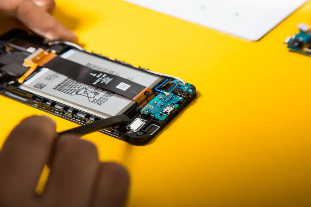 A technician Removing the Charge Port of a samsung mobile ontop of a yellow background